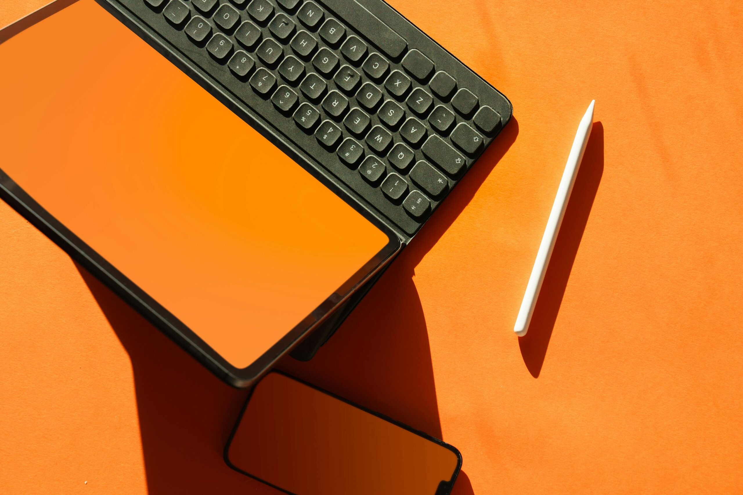 Stylish top-down view of a tablet with keyboard, smartphone, and stylus on a bright orange backdrop.